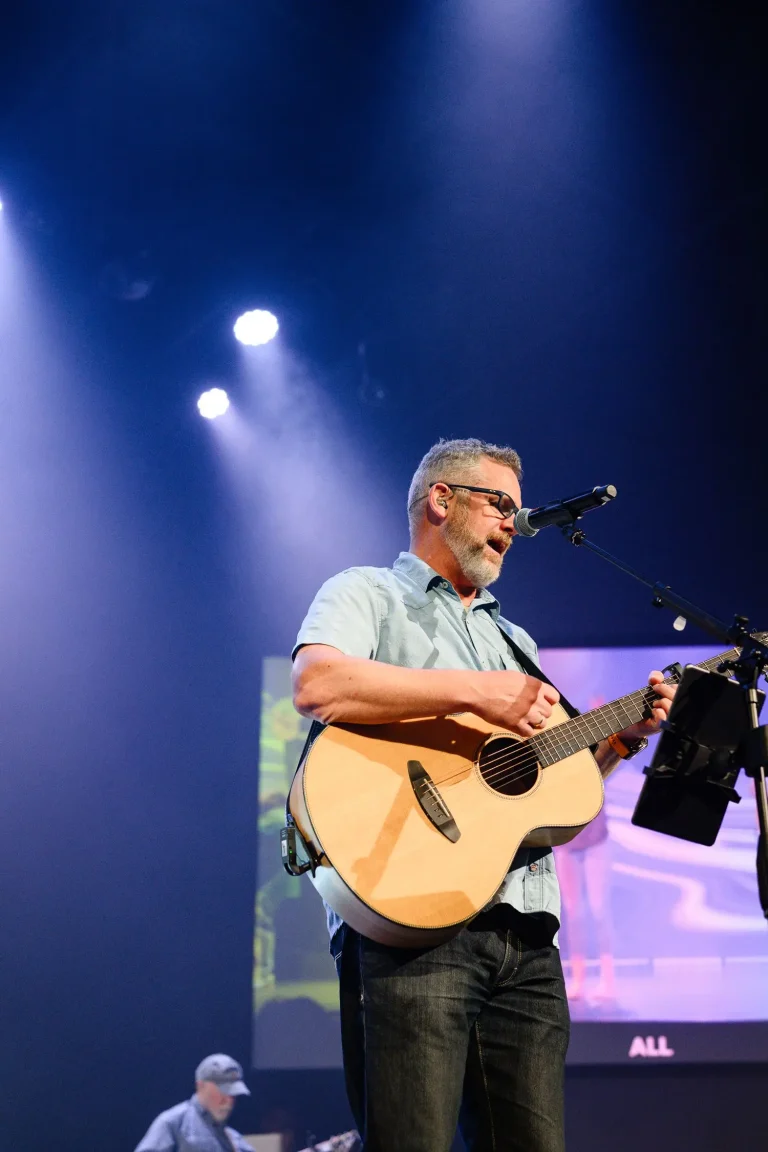 a man singing and playing a guitar on stage during a worship service