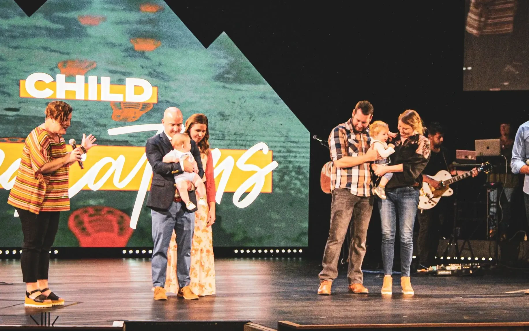 two groups of families being prayed over on a stage