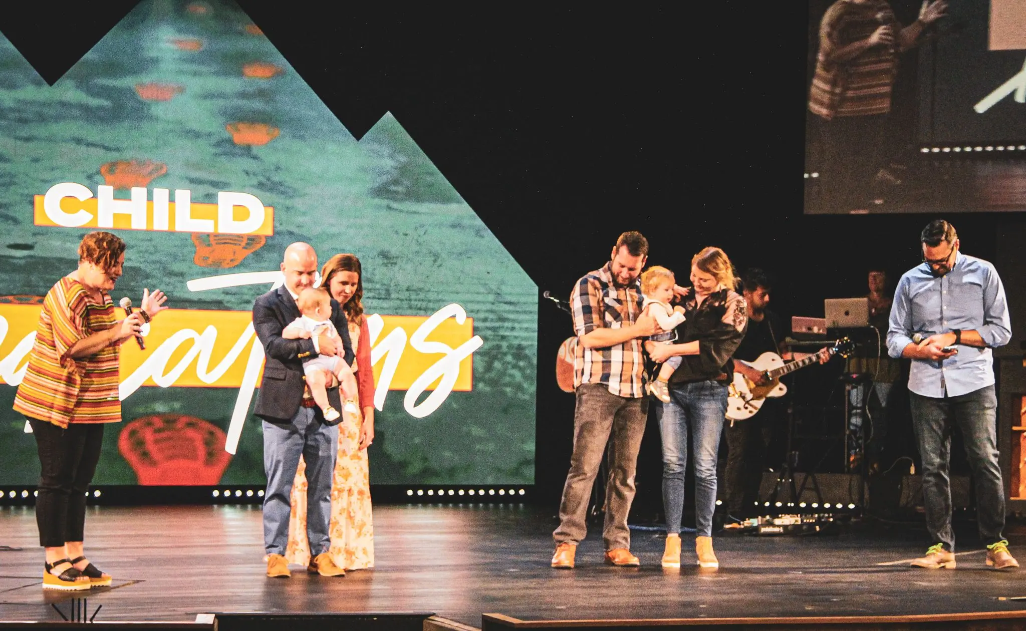 two groups of families being prayed over on a stage