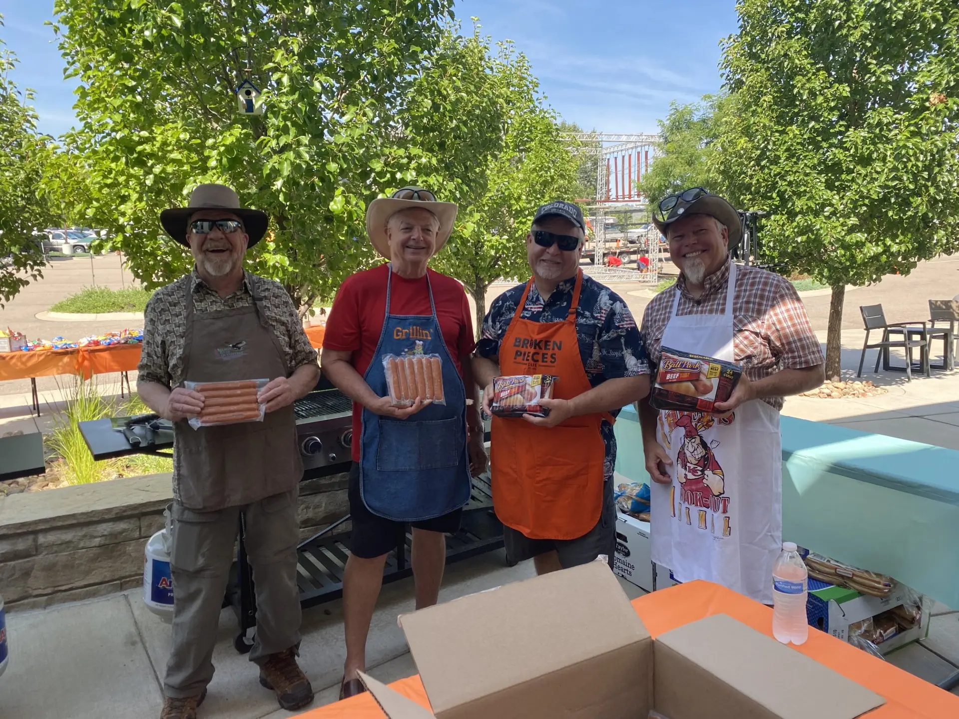 four men holding up hotdogs ready to be grilled