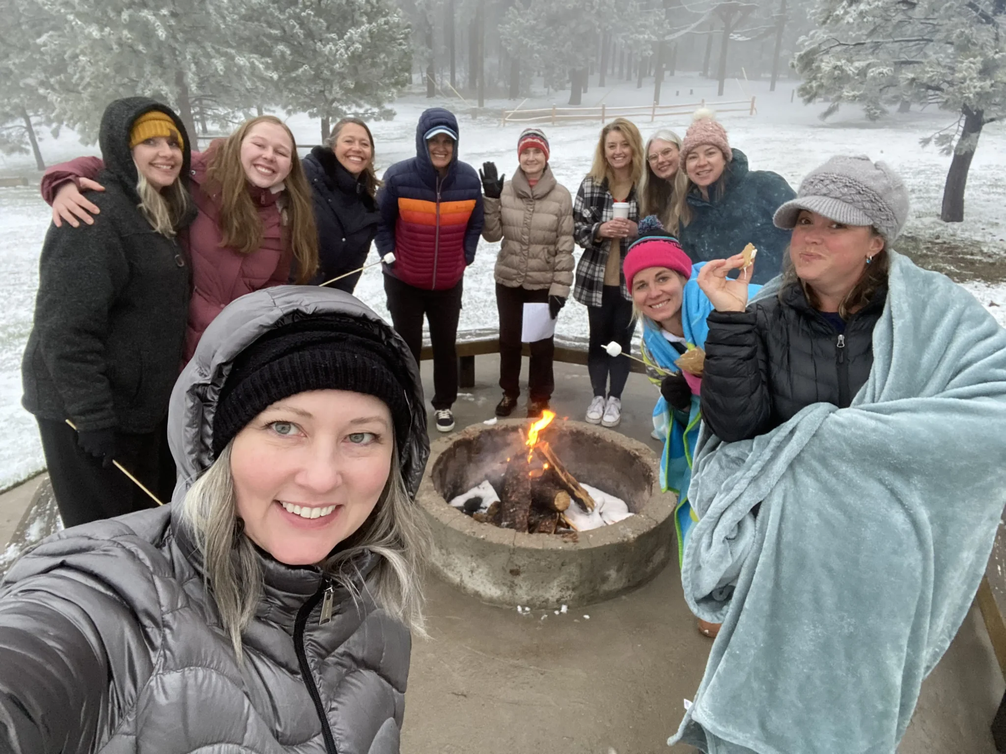 a group of women in the snow, gathered around a fire pit